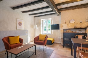 A living room with a sofa, armchair, coffee table, TV, and a dining area with chairs and a table.
