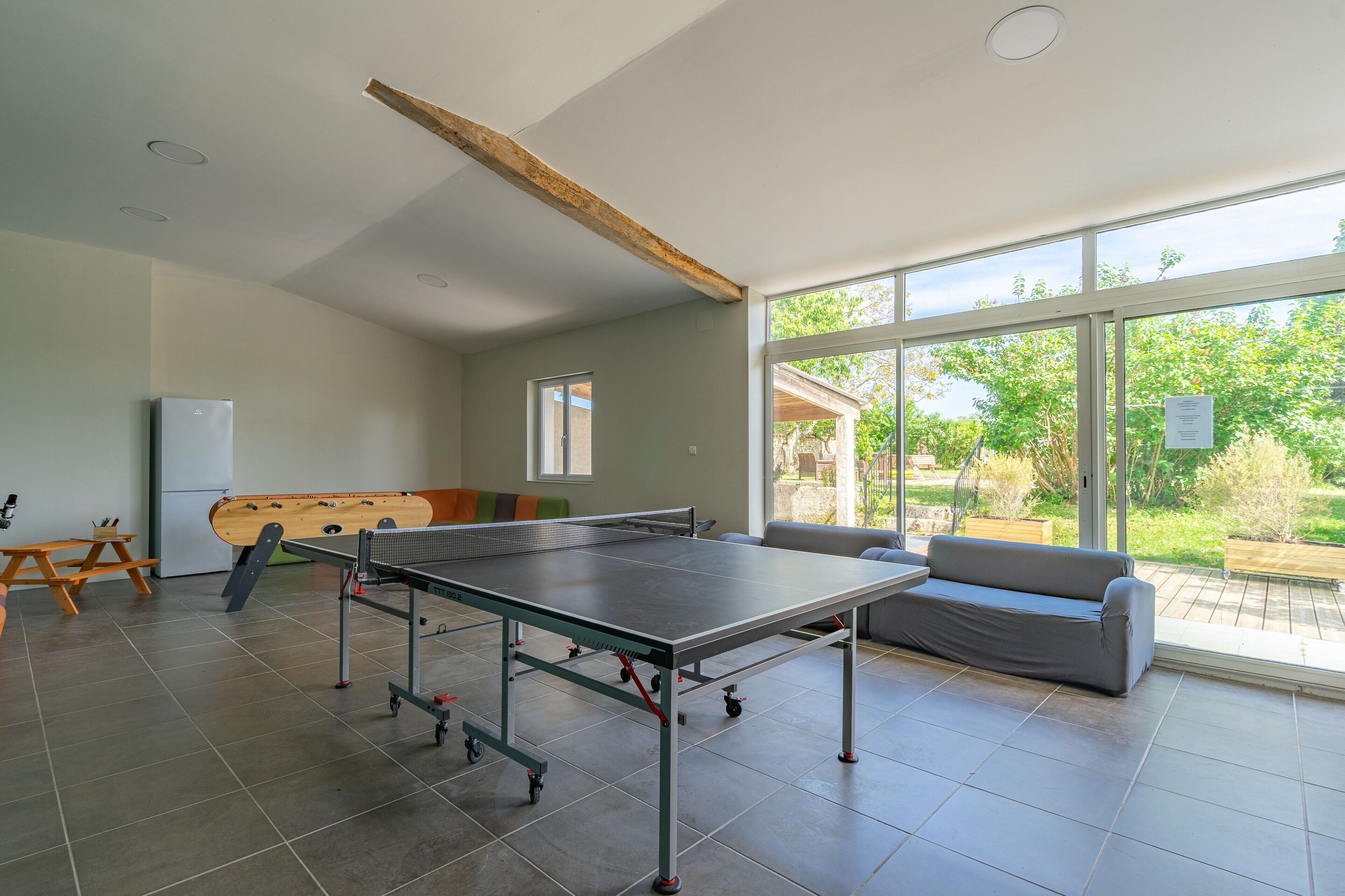Une pièce spacieuse équipée d’une table de ping-pong, d’un canapé et d’une fenêtre donnant sur l’extérieur.