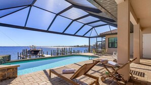 Ein Poolbereich mit freiem Blick auf das Meer, Holzliegen und eine überdachte Terrasse.