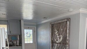 Una cocina con armarios blancos, piso de madera, un banco y una decoración rústica en la pared.