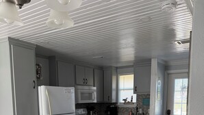 Una cocina compacta con armarios blancos, un refrigerador, microondas y estufa. Hay una mesa de comedor con sillas y una pequeña mesa azul.