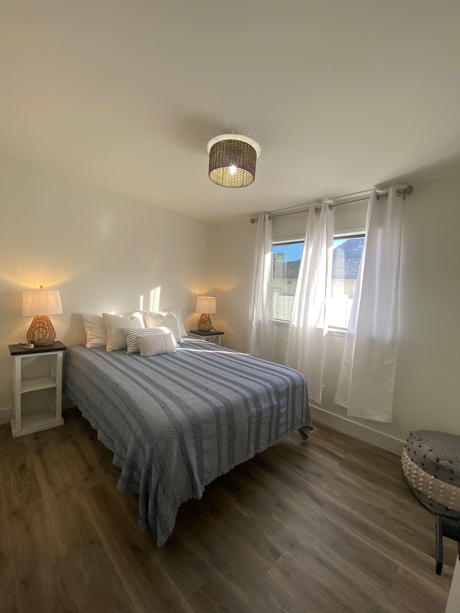 Une chambre à coucher comprenant un lit, deux tables de chevet, un luminaire suspendu et une fenêtre avec des rideaux.