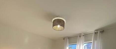 A bedroom with a bed, two bedside tables, a hanging light fixture, and a window with curtains.