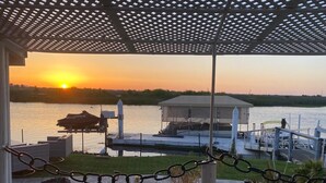 Ein Pavillon mit Blick auf einen Sonnenuntergang über dem Wasser, eine Anlegestelle und ein kleines Boot.