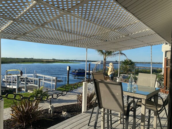 An outdoor patio with a view of the water, a covered seating area, and a dock with boats.