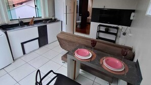 A compact kitchen with a dining area, a refrigerator, a television, and a window overlooking a residential area. - Furnished loft close to In the center with private garage. (Jardim Iririú Joinville)