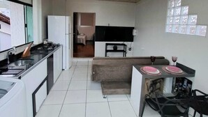 A modern kitchen with a central island, a dining area with a table and chairs, and a living space with a sofa. - Furnished loft close to In the center with private garage. (Jardim Iririú Joinville)