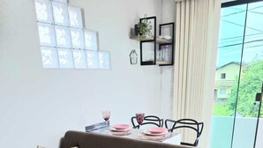 A modern living room with a brown sofa, a dining table with chairs, and a large window with a view of greenery. - Furnished loft close to In the center with private garage. (Jardim Iririú Joinville)