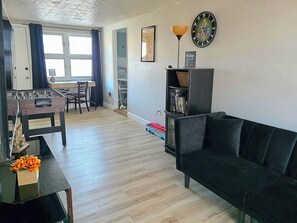 Un salon comprenant un canapé, une table à manger avec des chaises, un baby-foot, une bibliothèque et une horloge murale.