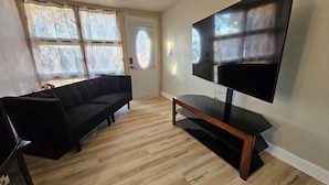 Un salon avec un canapé noir, une table basse en bois et un téléviseur à écran plat fixé au mur.