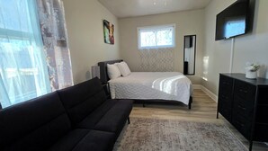 Une chambre à coucher comprenant un lit, un canapé, une télévision, un ventilateur de plafond, une fenêtre avec des rideaux et une commode.