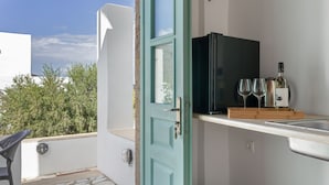 A balcony with a door leading to a kitchen area, a table, and a view of greenery.