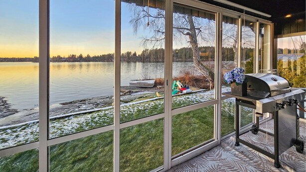 Ein Zimmer mit großen Fenstern, die auf einen See blicken, einem Grill und einer Aussicht auf einen Steg mit Booten.