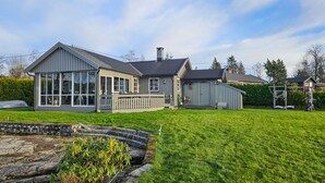 Ein großes, zweistöckiges Haus mit einer überdachten Terrasse, einem umzäunten Garten und einer Steinmauer.