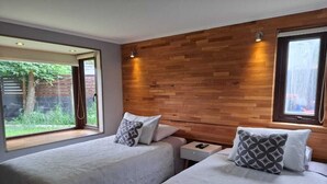 Un dormitorio con dos camas, cabecero de madera, una mesita de noche y ventana con vistas a zonas verdes.