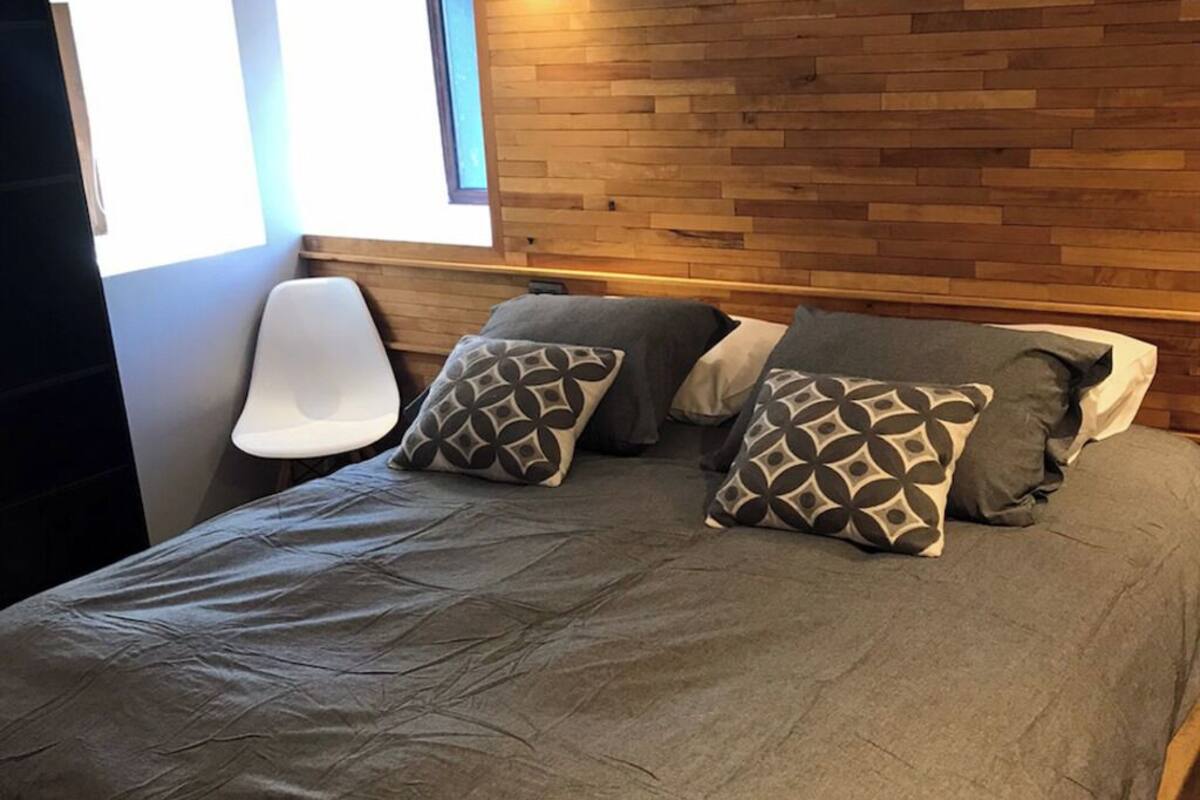 Ein Schlafzimmer mit einem hölzernen Kopfteil, einer grauen Bettdecke und gemusterten Kissen.