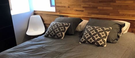 A bedroom with a wooden headboard, a grey bedspread, and patterned pillows.