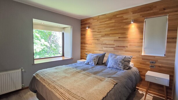 Un dormitorio con una cama grande, cabecera de madera, una ventana y una mesita de noche.