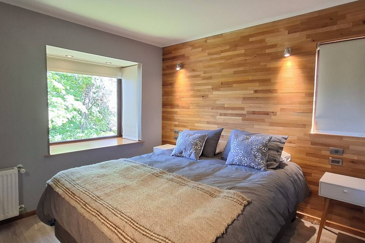Ein Schlafzimmer mit einem großen Bett, einem Holzkopfstück, einem Fenster und einem Nachttisch.
