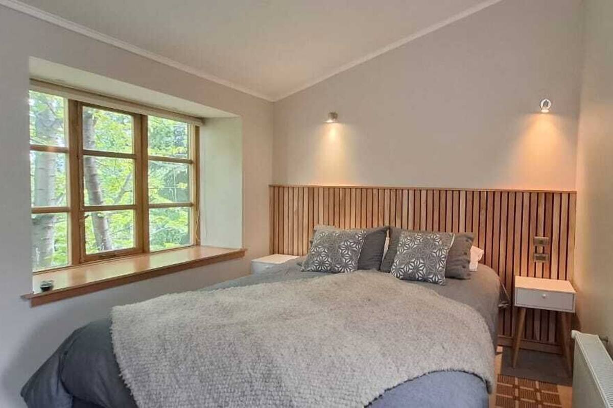 Ein Schlafzimmer mit einem großen Bett, einem Fenster mit vielen Sprossen, einem hölzernen Kopfteil und zwei Wandleuchten.