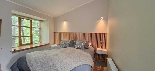 Une chambre à coucher avec un grand lit, une fenêtre à carreaux, une tête de lit en bois et deux lampes fixées au mur.
