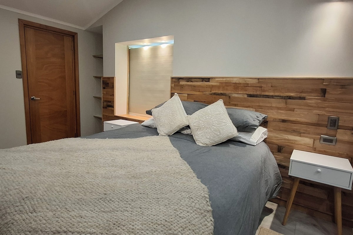 Ein Schlafzimmer mit einem Bett, Nachttischen, einem Kopfende aus Holz und einem Spiegel.