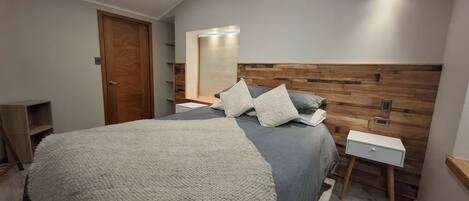 A bedroom with a bed, bedside tables, a nightstand, a wooden headboard, a mirror, and a door.