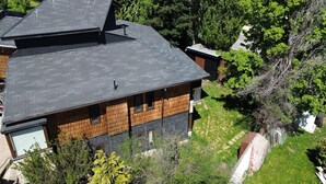Una casa de dos pisos con techo inclinado, rodeada de árboles y un patio cubierto de césped.