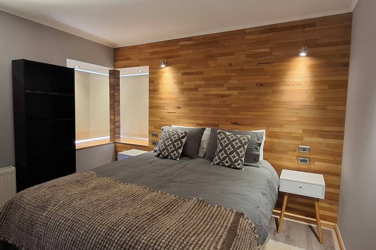 Ein modernes Schlafzimmer mit einem großen Bett, einer Wand aus Holzpaneelen, Nachttischen und einem Kleiderschrank.