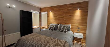 Un dormitorio moderno con una cama grande, panel de pared de madera, mesitas de noche y un armario.