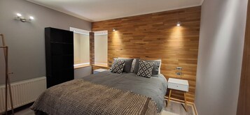Un dormitorio moderno con una cama grande, panel de pared de madera, mesitas de noche y un armario.