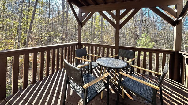 A wooden deck with a covered area, furnished with chairs and a table, overlooking a forested area. - Charming Private Studio in the Heart of Jasper (Jasper)