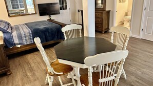 A room with a bed, a TV, a dining table with chairs, a dresser, and a bathroom visible through an open door. - Charming Private Studio in the Heart of Jasper (Jasper)