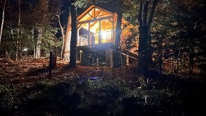 Una cabaña de estructura de madera, rodeada de árboles y un suelo boscoso.
