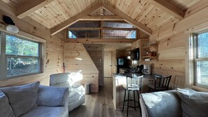 Interior de una cabaña con habitación en entrepiso, kitchenette y zona de estar con dos sofás.
