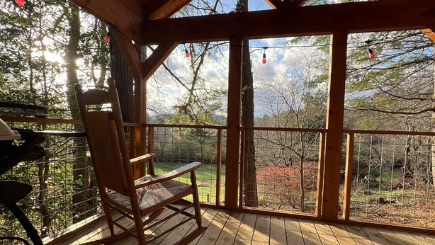 Una terraza de madera con una mecedora, una mesa y vistas a un área boscosa.