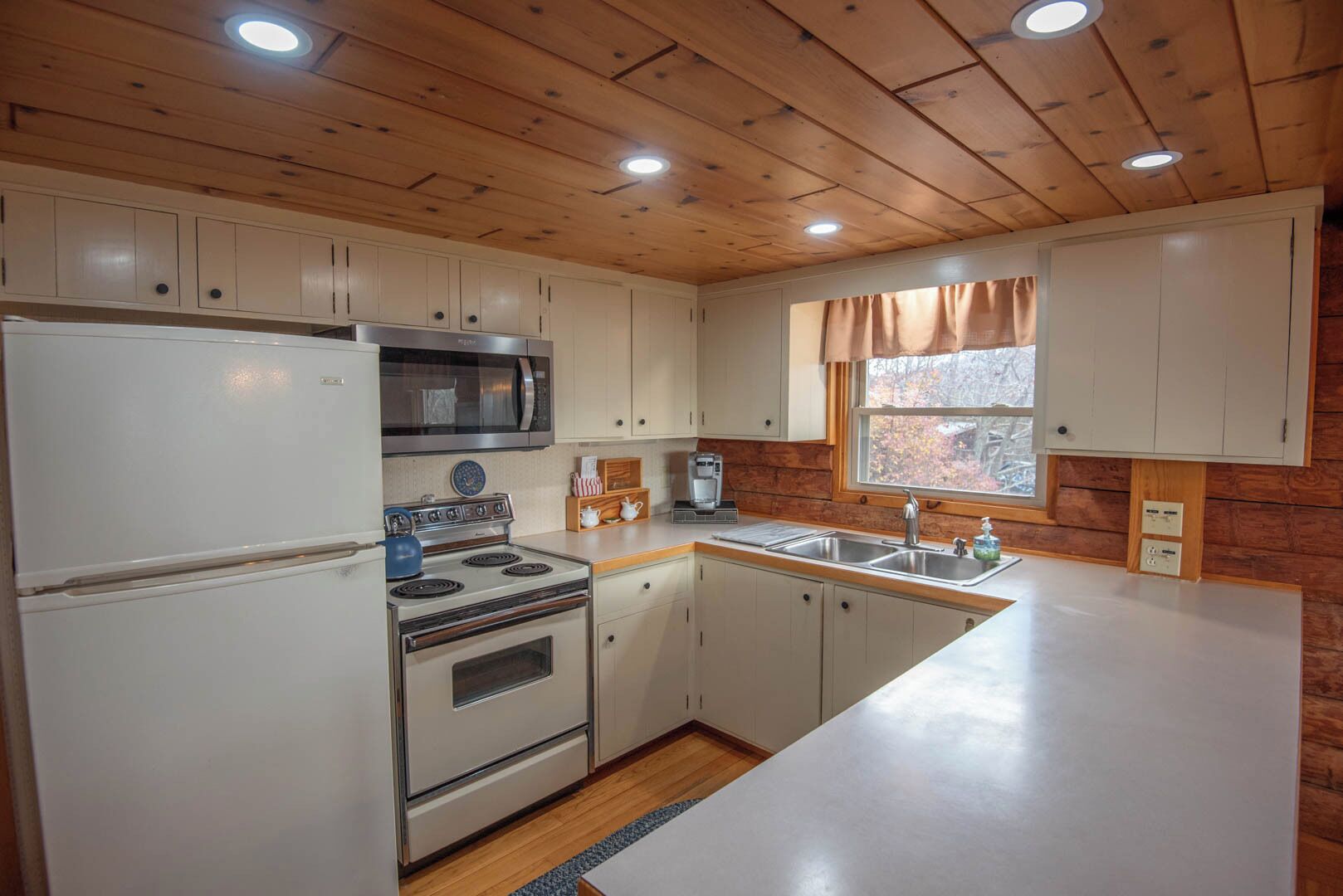 A compact kitchen with white cabinets, a microwave, stove, and sink.