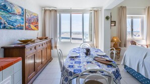 A dining area with a table set for two, a view of the beach, and a wooden cabinet with dishes. - Cosy apartment for 4 guests with WIFI, A/C, TV, patio and pets allowed (San Vincenzo)