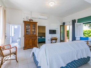 Une chambre à coucher comprenant un lit, une armoire en bois, un téléviseur et une fenêtre donnant sur un paysage verdoyant.
