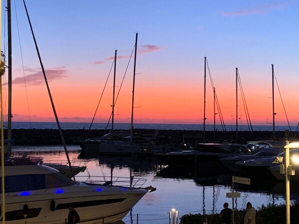 Un port de plaisance au coucher du soleil, avec des bateaux amarrés, une eau calme et un ciel dégagé.