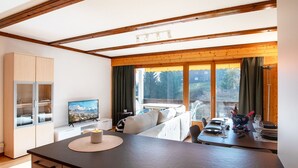 A modern kitchen with wooden cabinets, a dining area with a table set for two, and a large window with curtains. - Opale 24 by Interhome (Villars)