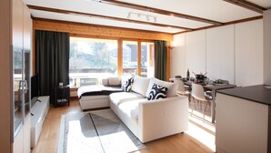 A modern living room with a sofa, a dining table, and a kitchen area. - Opale 24 by Interhome (Villars)