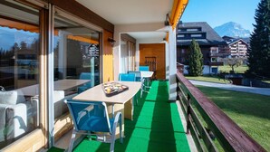 A balcony with a table and chairs, a green artificial turf floor, and a view of a mountain and buildings in the background. - Opale 24 by Interhome (Villars)