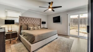 A bedroom with a tufted headboard, a large bed, a ceiling fan, a TV, and a sliding glass door to a backyard. - 6 Bed - Swimming Pool - Hot Tub - Prime Location (Irving)