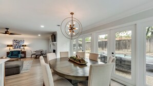 A modern dining area with a round table, white chairs, and a chandelier. - 6 Bed - Swimming Pool - Hot Tub - Prime Location (Irving)