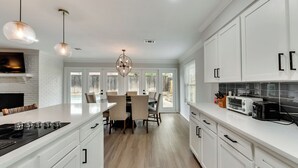 A modern kitchen with white cabinetry, a central island, and a dining area with chairs. - 6 Bed - Swimming Pool - Hot Tub - Prime Location (Irving)