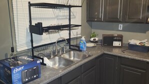 Uma cozinha com armários escuros, uma pia dupla, um escorredor de louça, uma caixa de detergente Oster e um rádio.