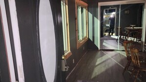 Quarto com porta de madeira escura, tapete estampado e área de jantar com cadeiras e mesa de madeira.