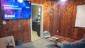 Quarto com paredes de madeira, uma TV exibindo um erro de conexão, um sofá azul, uma mesa de centro e um ventilador de teto.