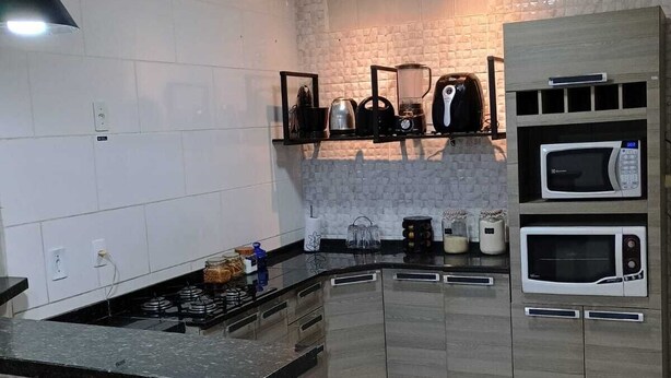 Een moderne keuken met een zwart aanrecht, een witte betegelde achterwand en houten kastjes.